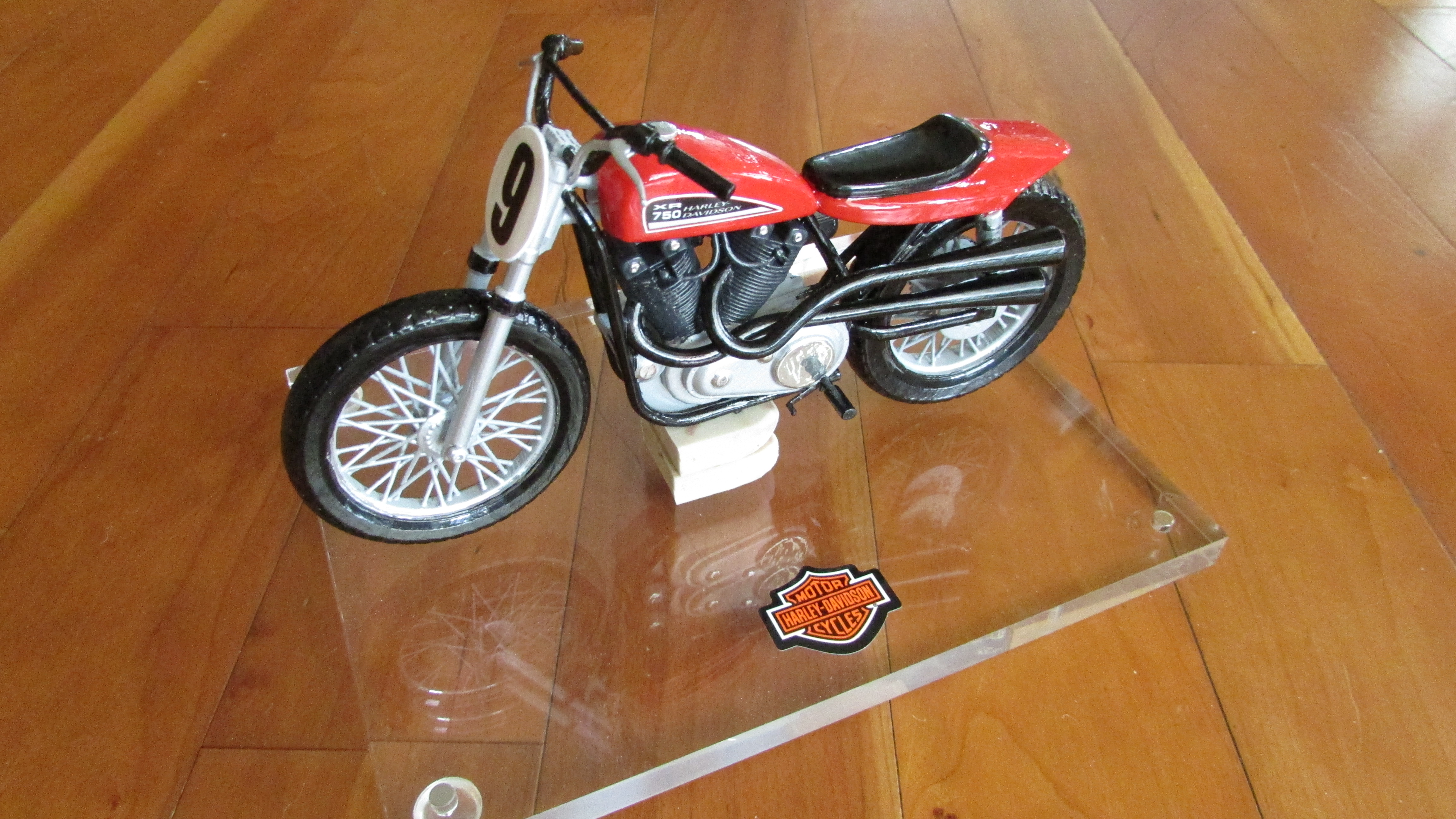 Red Harley-Davidson 750 model motorcycle with black seat, spoked wheels, and a number 9 front plate on a clear base.